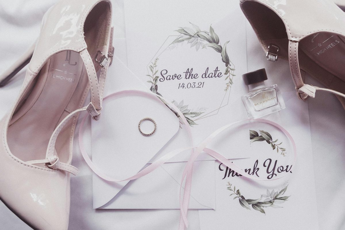 Flatlay mit Save-the-Date-Karte, Ring, Schuhen und Hochzeitspapeterie