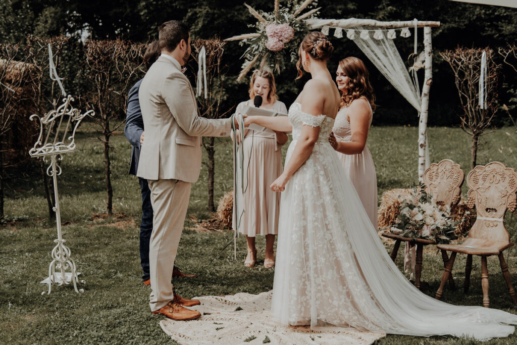 Freie Trauung unter Traubogen im Boho-Stil mit Brautpaar, Traurednerin und Brautjungfer – Hochzeitskonzept mit Zeremonieplanung und Checkliste für persönliche Hochzeit.