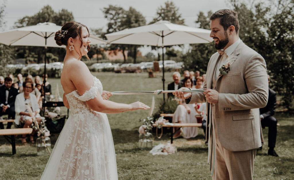 Brautpaar bei freier Trauung im Garten, hält gemeinsam ein Band beim Hochzeitsritual – emotionale Hochzeitszeremonie als Teil des Hochzeitskonzepts und Checkliste für unvergessliche Momente.