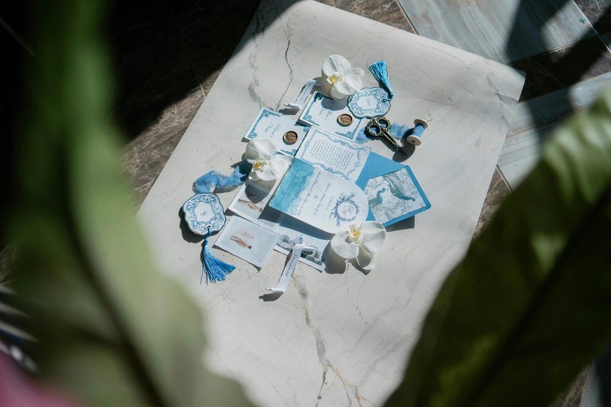 Moodboard mit blauer Hochzeitspapeterie, Siegel und Orchideen auf einem Tisch