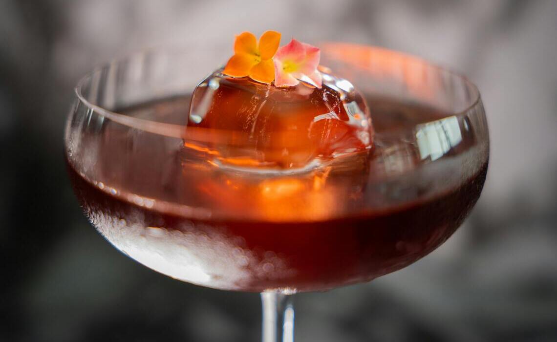 Eleganter Signature Drink für Hochzeiten in einer Coupette mit Eisblock und Blütendekoration als stilvoller Hochzeitscocktail