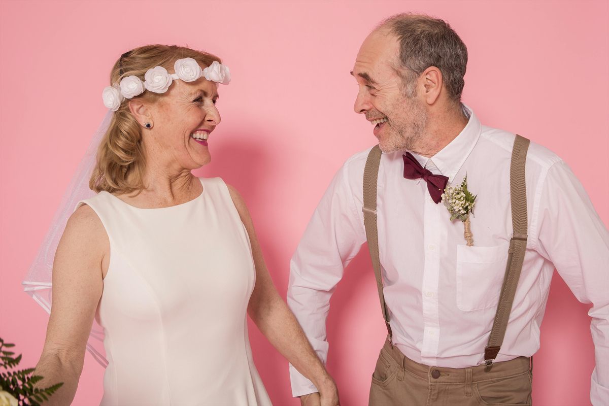 Locker gekleidetes älteres Paar in Hochzeitsoutfits vor rosa Hintergrund