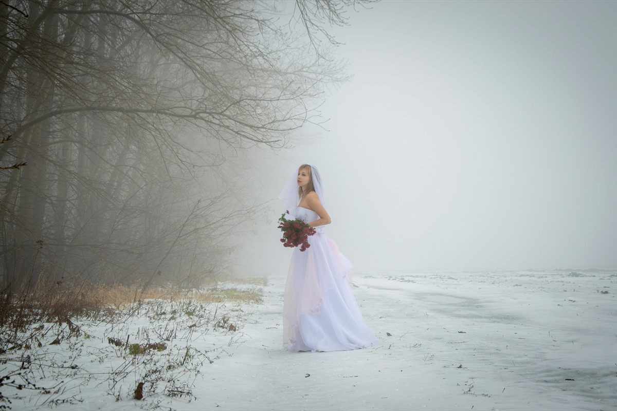 Braut mit rotem Bouquet auf verschneitem Weg im Nebel