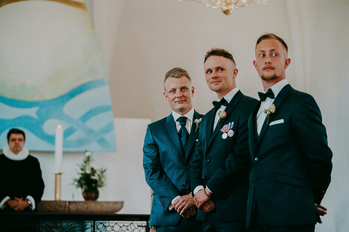 Drei Männer in dunklen Anzügen bei einer kirchlichen Trauung vor dem Altar